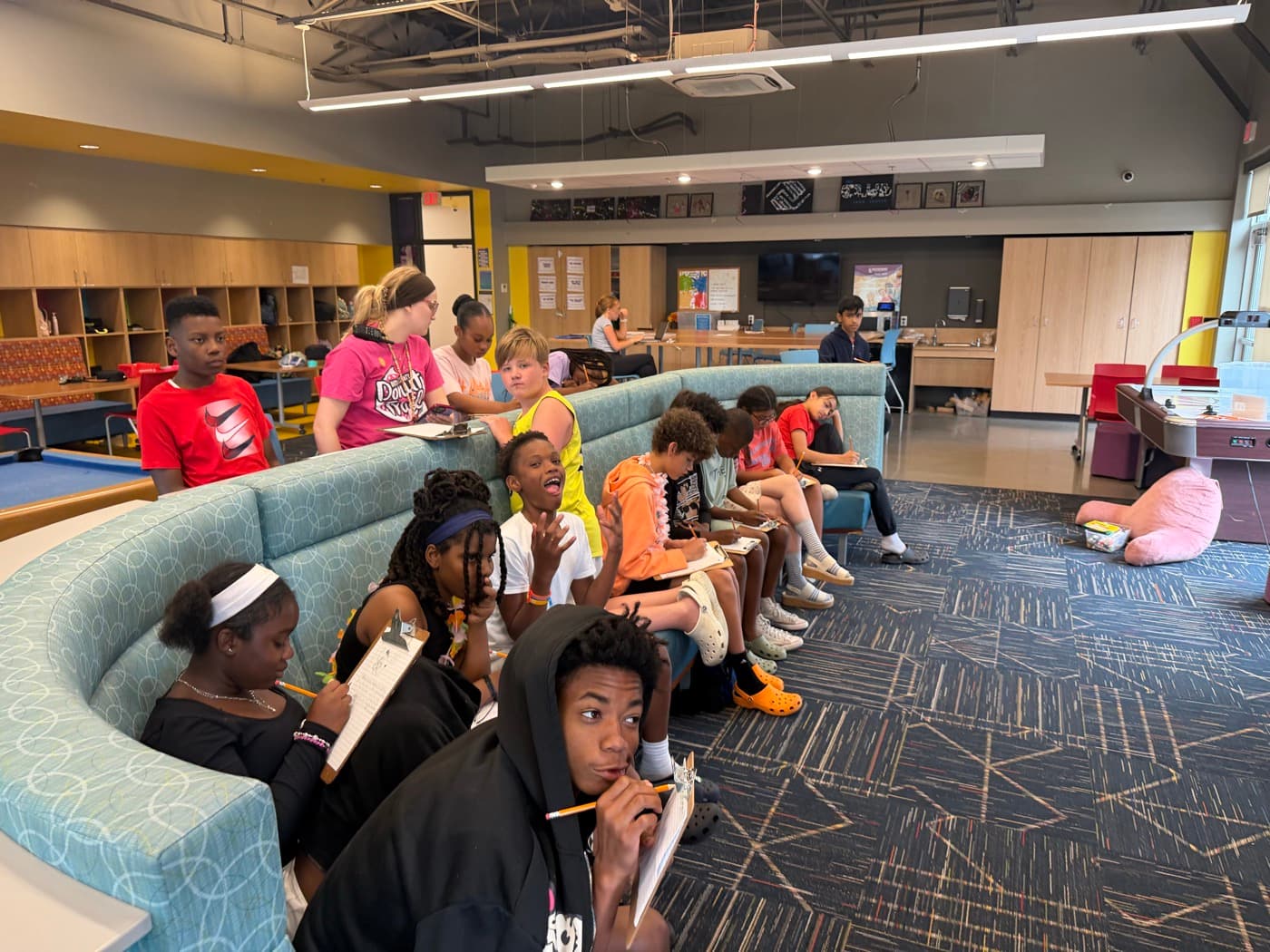 Students taking notes on clipboards, one raising a hand to answer